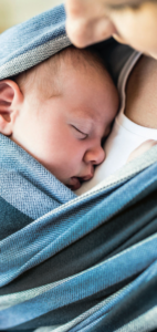 Baby in Tragetuch auf Brust einer Frau. Gesicht Frau im Seitenprofil zu sehen